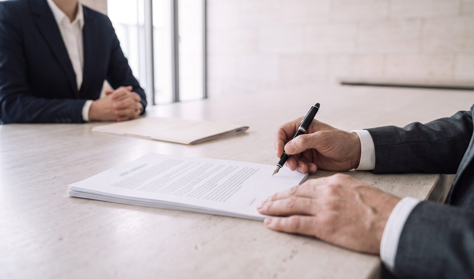 Un dirigeant s’apprête à signer un accord au stylo plume, face à une interlocutrice.